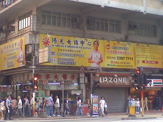 A bright yellow banner featuring a smiling woman hung above retail shops on a busy street in Hong Kong. The words on the poster promote a domestic worker services such as cleaning and in-home care, a popular profession for Filipino migrants.