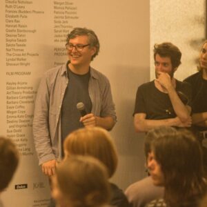 Joel Stern holding a microphone against a wall listing names at an event with other people