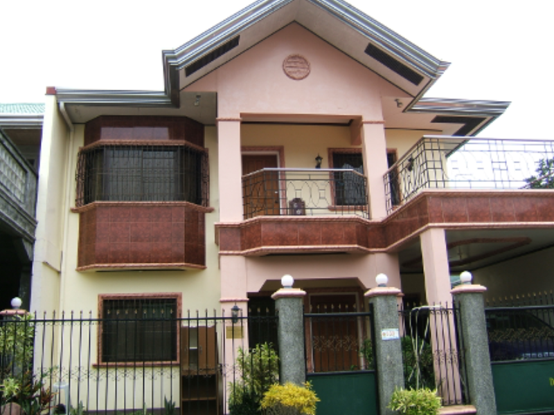 A pink and white pastel two-story house is boarded up. With large columns and brown marble tiles, the architecture draws inspiration from an Italian villa. The house is owned by a Filipino migrant, the Italian-inspired architecture indicating that the owner works overseas. 