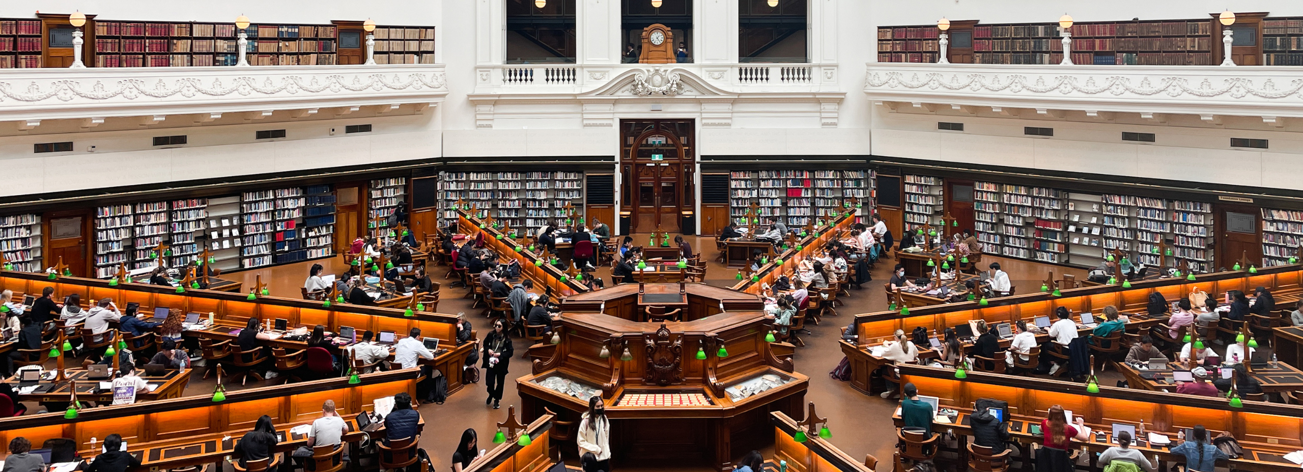 A wide-angle shot of the reading room in the State Library of Victoria which shows the angular desks and central catalogue desk in an artful geometric pattern.