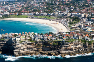 An aerial shot of Bondi beach, showing significant height of the Bondi Cliffs and the large houses built along the outcrop. 