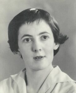 A old black and white headshot of Brenda Niall in her early twenties. She has large brown eyes and short dark hair. She wears a white collared shirt. 