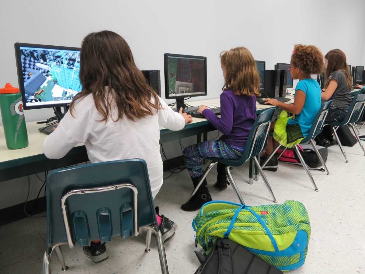 A group of school primary school children play Minecraft on computers in a classroom. 