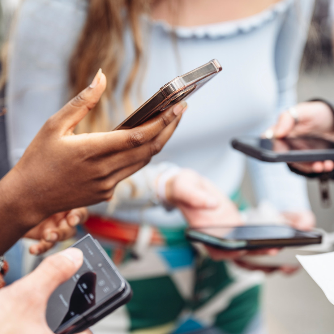 A group of young people hold smart phones. 