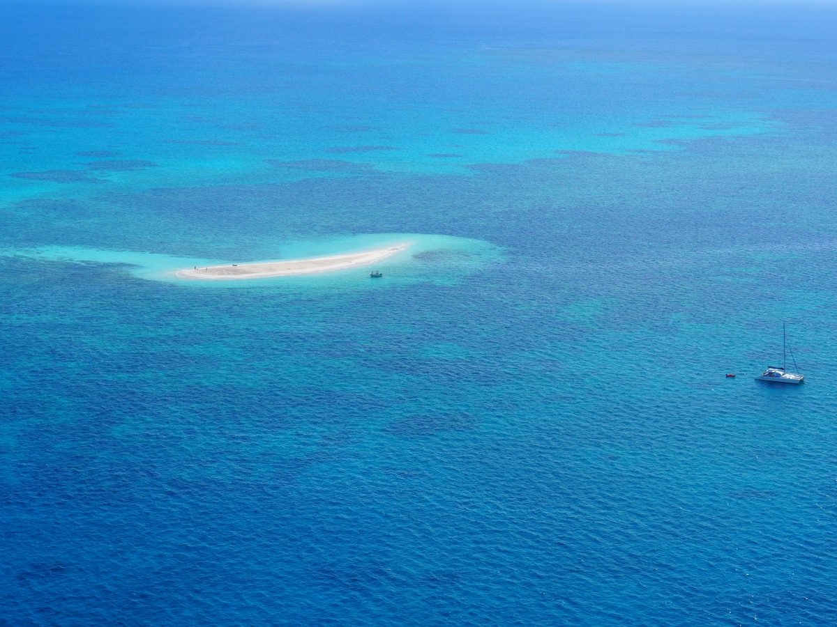 Different shades of blue sea with a small island of sand. Two boats on the water.