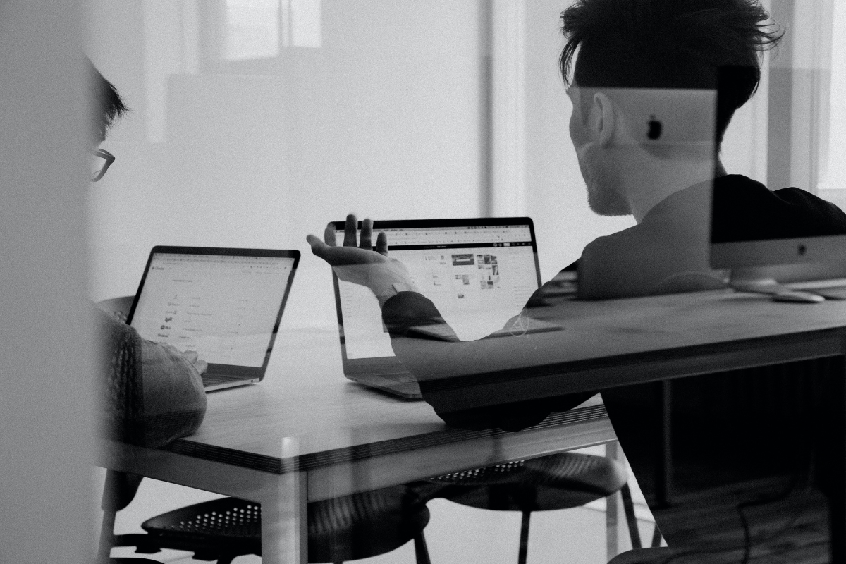 An image of a two men discussing a topic while using laptops